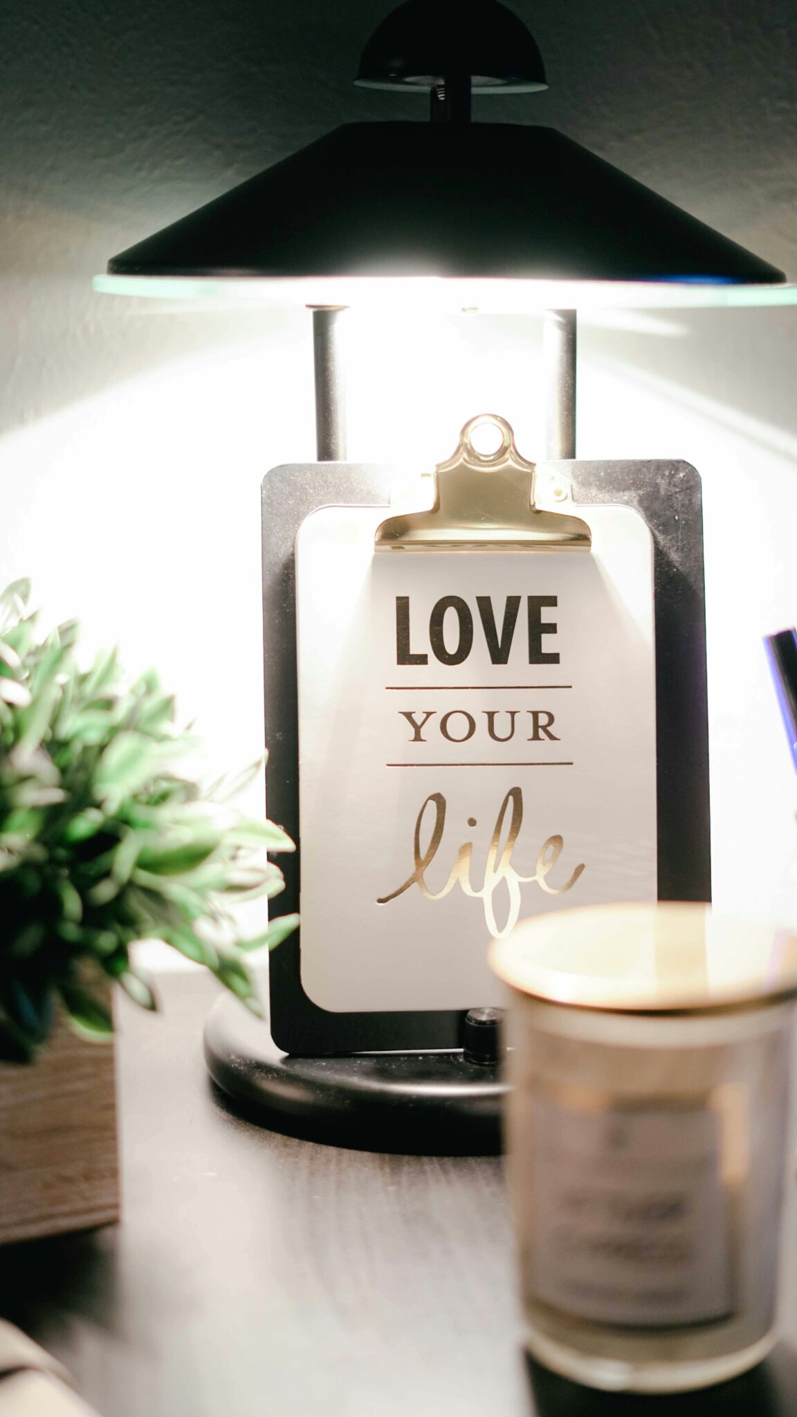 Home A warmly lit desk setup featuring a lamp, inspirational clipboard, and decor for a cozy ambiance.